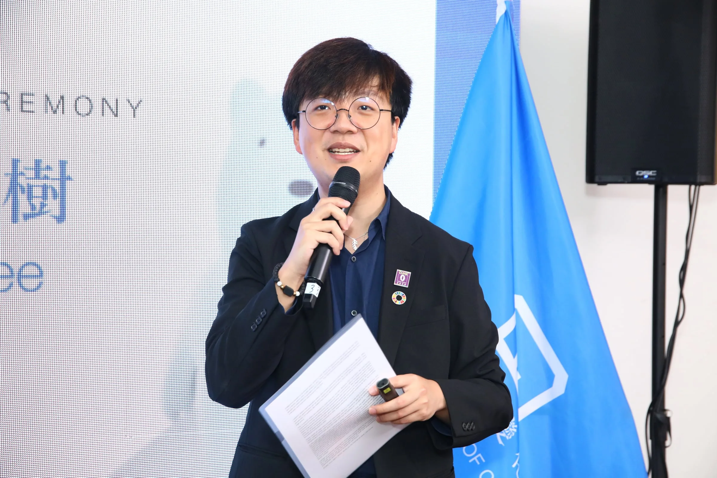 A speaker holding a microphone and notes on stage